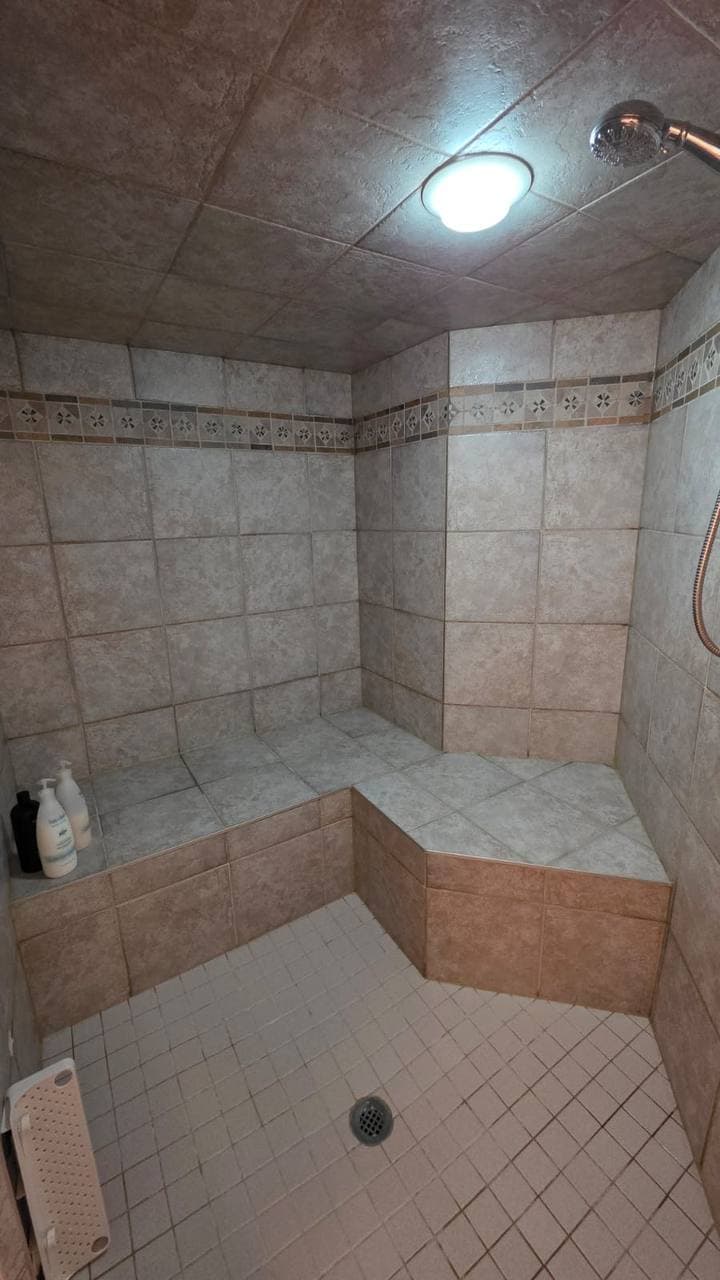 Dated beige tiled corner shower with bench before renovation, Calgary