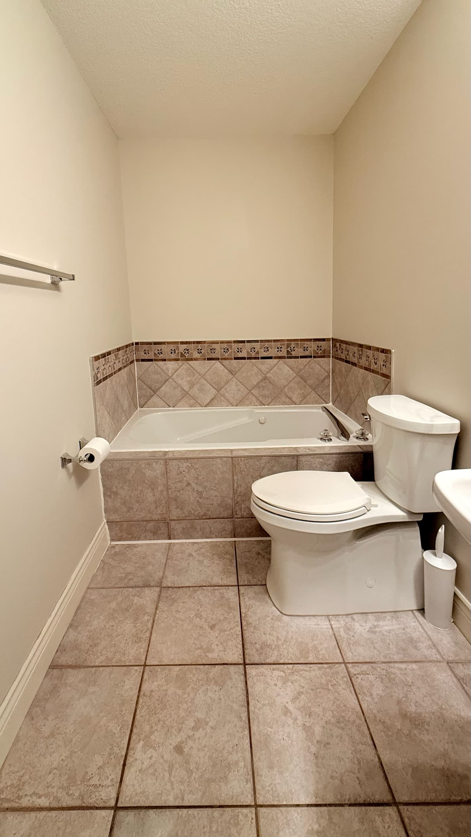 Dated bathroom with beige tile-surround tub and busy border before renovation, Calgary